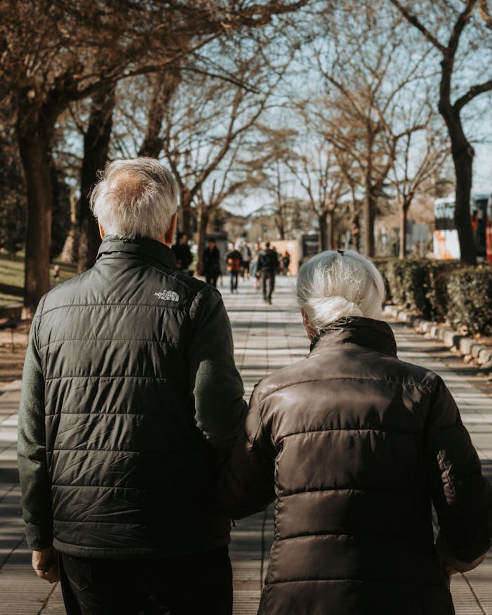 Senior couple walking hand in hand in a sunny Madrid park, embodying togetherness and tranquility.